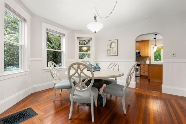 dining area with a wainscoted wall, plenty of natural light, arched walkways, and wood finished floors