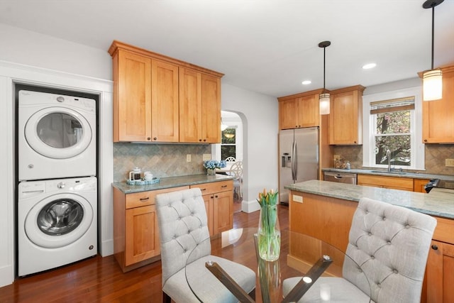 kitchen featuring appliances with stainless steel finishes, stacked washer / drying machine, a sink, arched walkways, and dark wood-style flooring