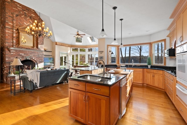 kitchen with sink, a brick fireplace, light hardwood / wood-style flooring, an island with sink, and decorative light fixtures