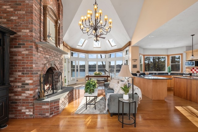 living room with sink, light hardwood / wood-style flooring, lofted ceiling with skylight, a fireplace, and a water view