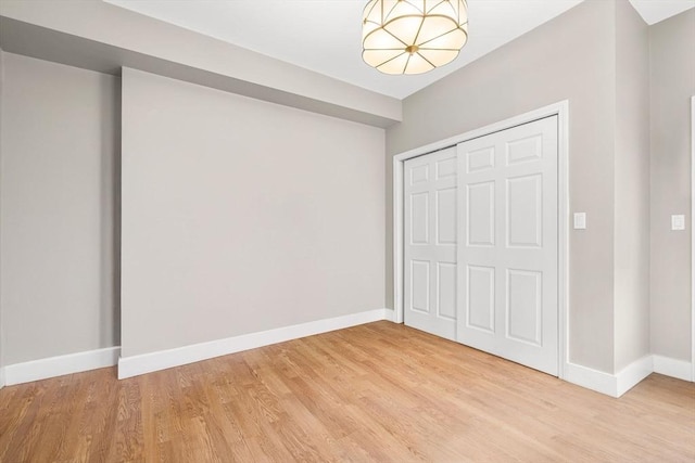 unfurnished bedroom with a closet, baseboards, a notable chandelier, and light wood-type flooring
