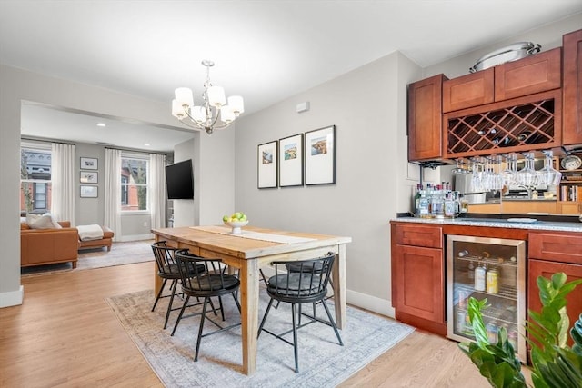 dining area featuring beverage cooler, baseboards, a bar, light wood-style flooring, and a notable chandelier