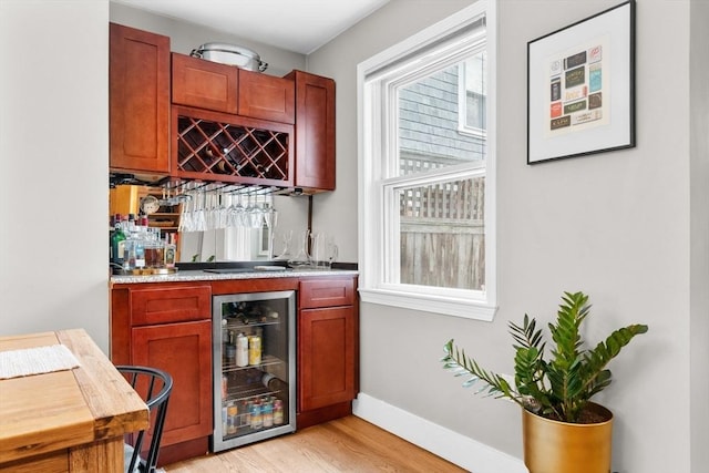 bar featuring beverage cooler, light wood-type flooring, baseboards, and indoor wet bar