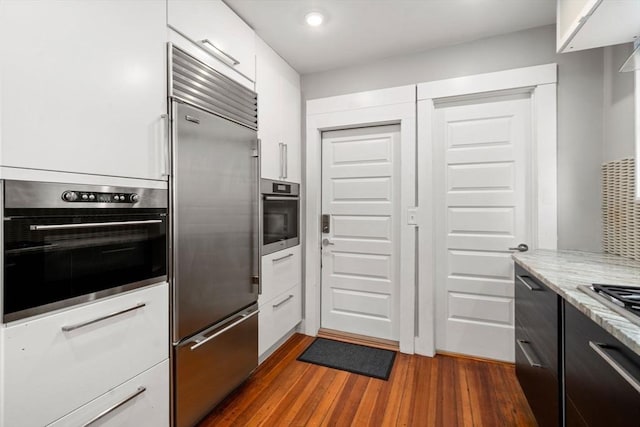 117 Sycamore St Unit 1, Boston, MA 02131 - kitchen with appliances with stainless steel finishes, dark wood-style flooring, white cabinets, light stone counters, and recessed lighting