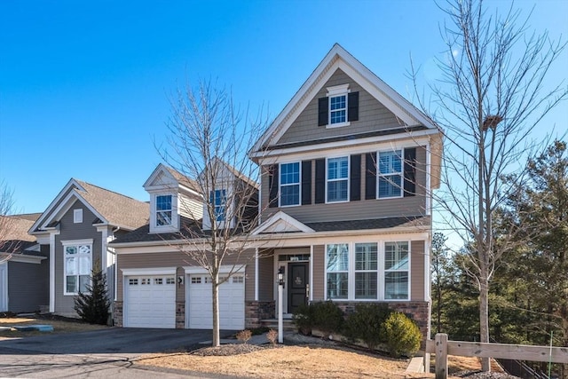 view of front of property featuring a garage, stone siding, driveway, and fence