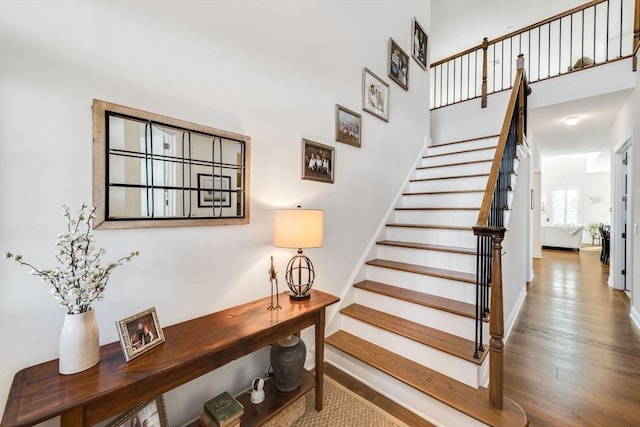 stairway with wood finished floors, baseboards, and a towering ceiling