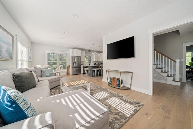 living area featuring plenty of natural light, light wood-style flooring, baseboards, and stairway