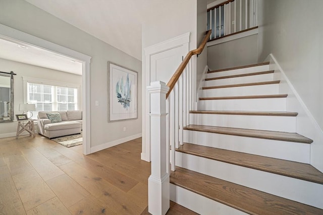stairs featuring a barn door, baseboards, and hardwood / wood-style floors