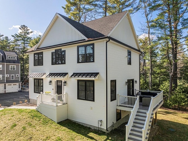 rear view of property with board and batten siding, a standing seam roof, a lawn, a shingled roof, and stairs