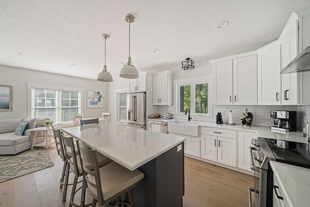 kitchen featuring a sink, stainless steel appliances, open floor plan, a kitchen bar, and backsplash