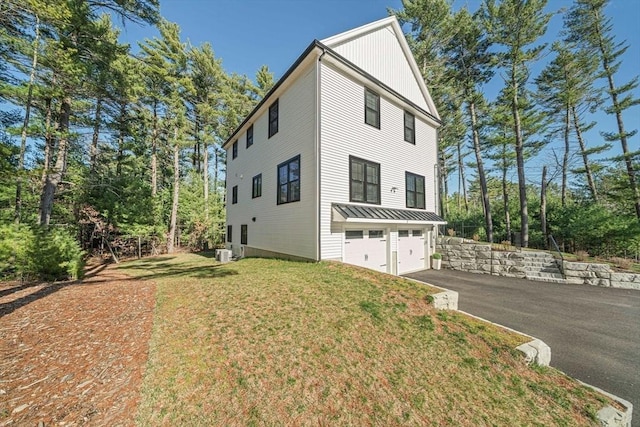 view of side of home with a yard, an attached garage, cooling unit, and aphalt driveway