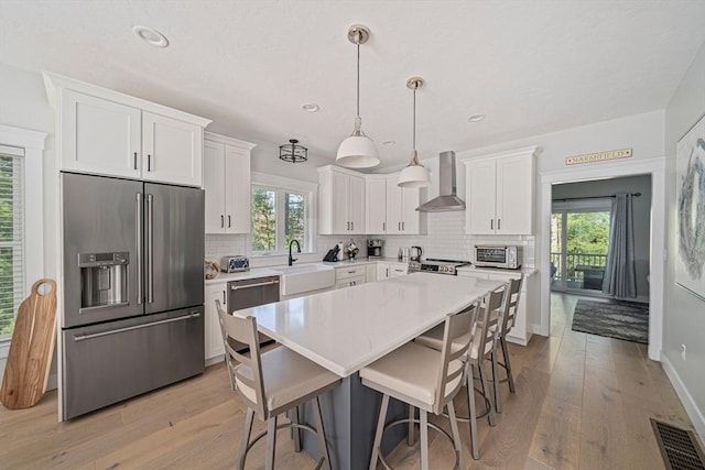 kitchen featuring appliances with stainless steel finishes, a sink, wall chimney exhaust hood, tasteful backsplash, and visible vents