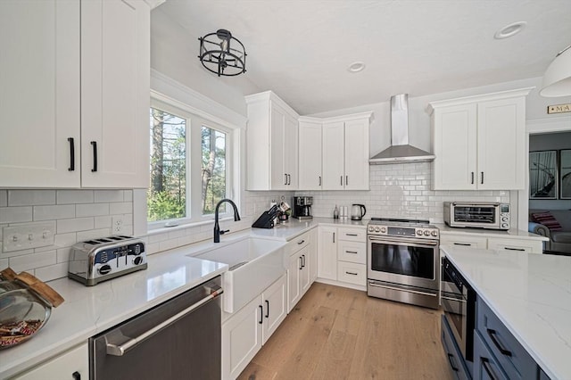 kitchen featuring appliances with stainless steel finishes, a sink, wall chimney exhaust hood, white cabinetry, and a toaster