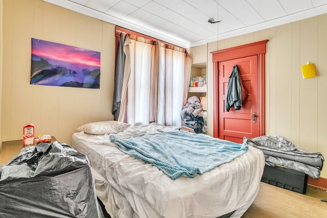 bedroom featuring ornamental molding, wood walls, and hardwood / wood-style floors