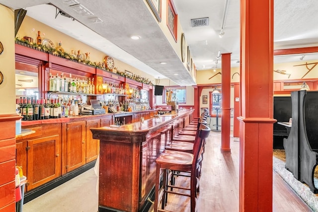 bar featuring pendant lighting, light hardwood / wood-style floors, track lighting, a textured ceiling, and decorative columns