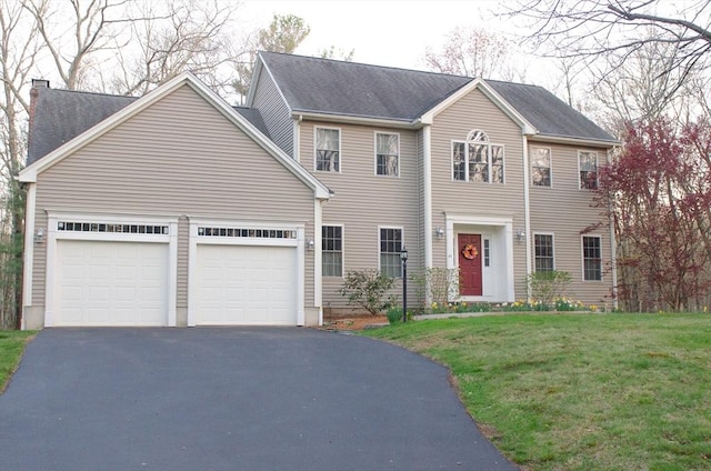 colonial-style house with asphalt driveway, a garage, a front lawn, and a chimney