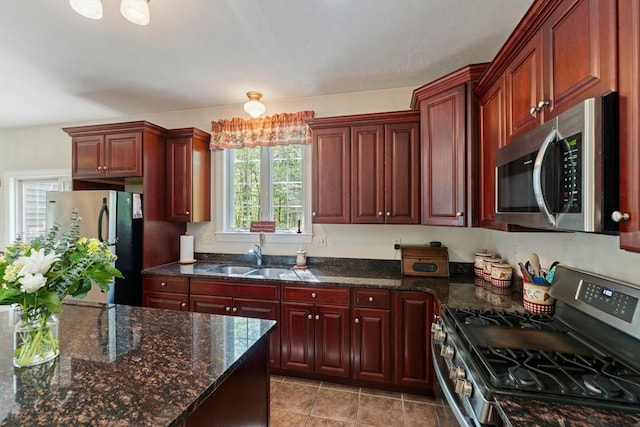 kitchen featuring appliances with stainless steel finishes, a sink, dark brown cabinets, and dark stone counters