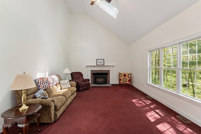 living room featuring a ceiling fan, dark colored carpet, baseboards, a brick fireplace, and a skylight