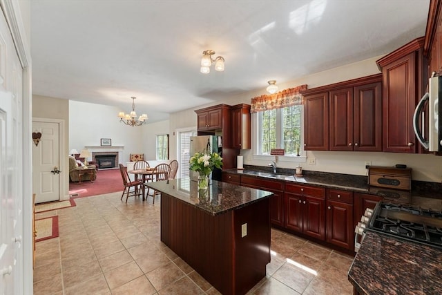 kitchen featuring appliances with stainless steel finishes, a sink, a chandelier, light tile patterned flooring, and a center island