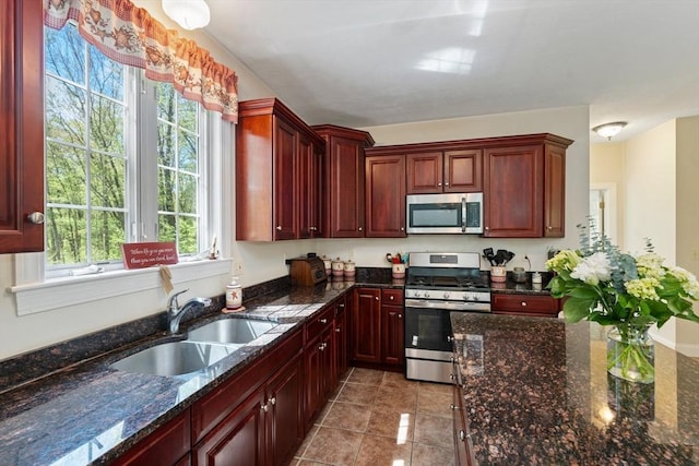 kitchen with stainless steel appliances, a sink, reddish brown cabinets, light tile patterned flooring, and dark stone counters