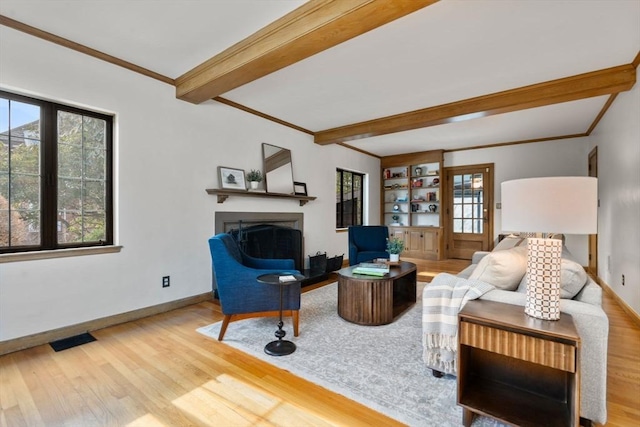 living room with beamed ceiling, ornamental molding, a healthy amount of sunlight, and light wood-type flooring