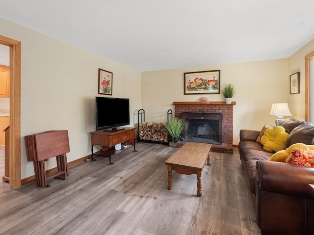 living room with a brick fireplace, baseboards, and wood finished floors