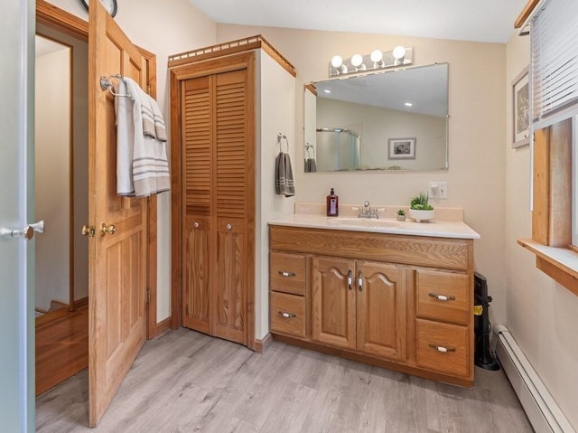 bathroom featuring a closet, wood finished floors, baseboard heating, and vanity