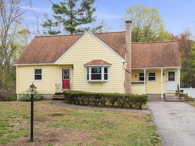 view of front of home with roof with shingles, a chimney, and a front lawn