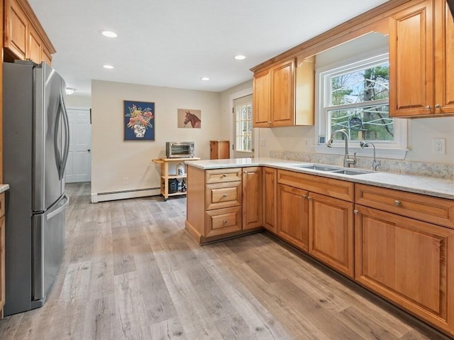 kitchen featuring a sink, freestanding refrigerator, a baseboard heating unit, a peninsula, and light wood-style flooring