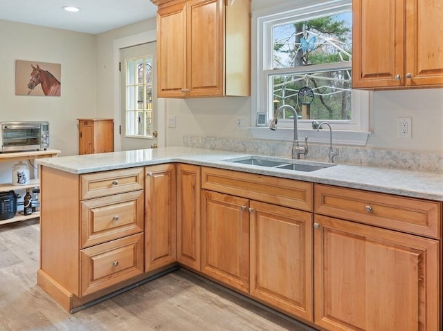 kitchen with light stone counters, a sink, a peninsula, light wood-type flooring, and a toaster