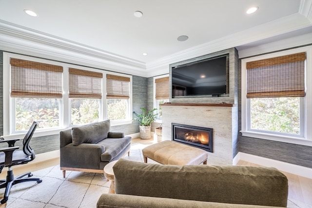 living room with a large fireplace, a healthy amount of sunlight, ornamental molding, and light hardwood / wood-style flooring