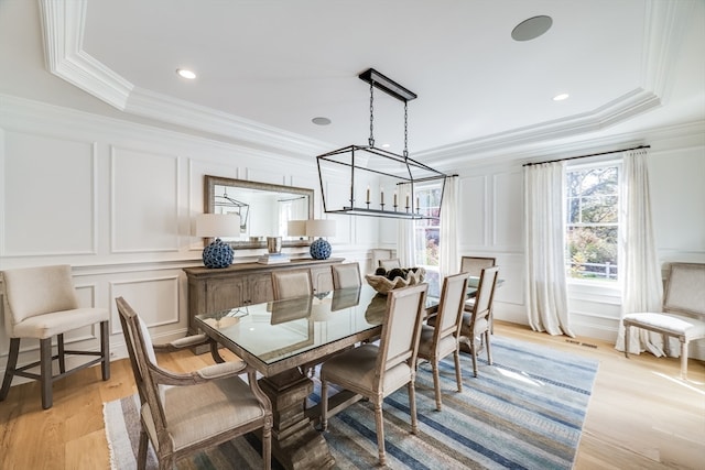 dining area featuring ornamental molding, light hardwood / wood-style floors, and a raised ceiling