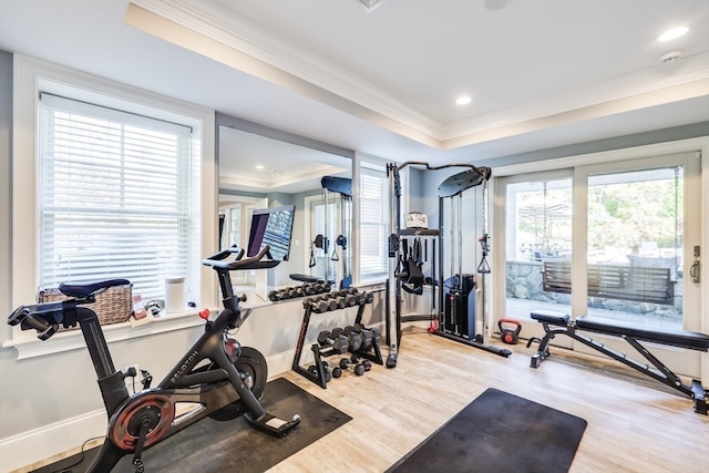 exercise room featuring crown molding, a raised ceiling, and light wood-type flooring