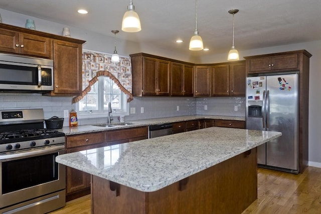 kitchen with appliances with stainless steel finishes, pendant lighting, sink, a kitchen breakfast bar, and a center island