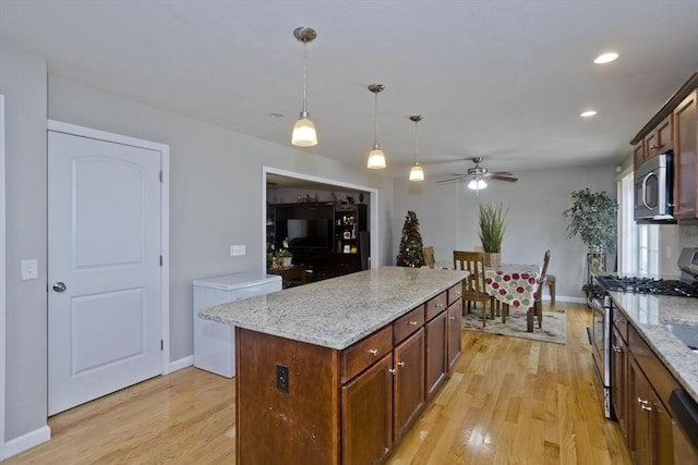 kitchen featuring light stone counters, decorative light fixtures, light hardwood / wood-style flooring, appliances with stainless steel finishes, and a kitchen island