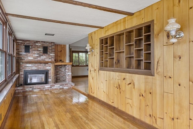 38 Lakeshore Dr, Wayland, MA 01778 - unfurnished living room featuring hardwood / wood-style floors, beamed ceiling, wooden walls, a fireplace, and a textured ceiling