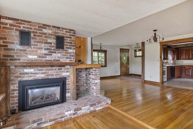 38 Lakeshore Dr, Wayland, MA 01778 - unfurnished living room with light wood-type flooring, baseboards, a brick fireplace, a chandelier, and a textured ceiling