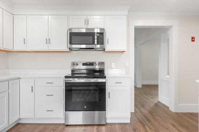 59 Altamont St, Haverhill, MA 01830 - kitchen with stainless steel appliances, light countertops, light wood-style floors, white cabinetry, and ornamental molding