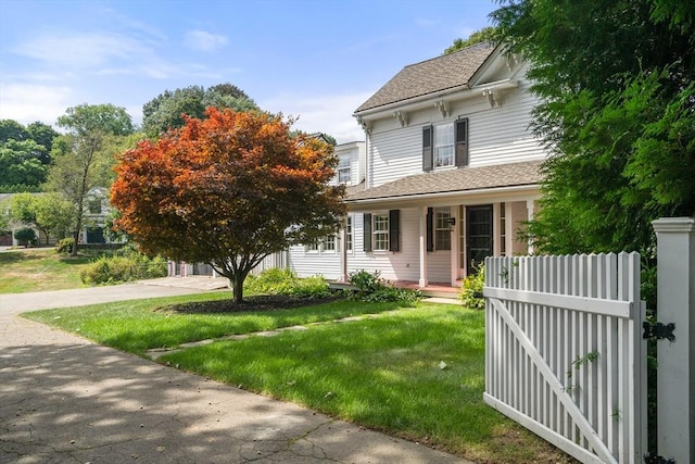 italianate-style house featuring a front lawn, a shingled roof, fence, and a gate