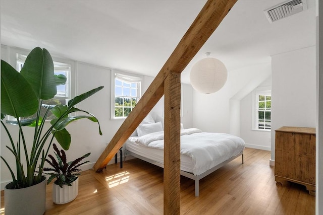 bedroom with multiple windows, visible vents, wood finished floors, and beamed ceiling