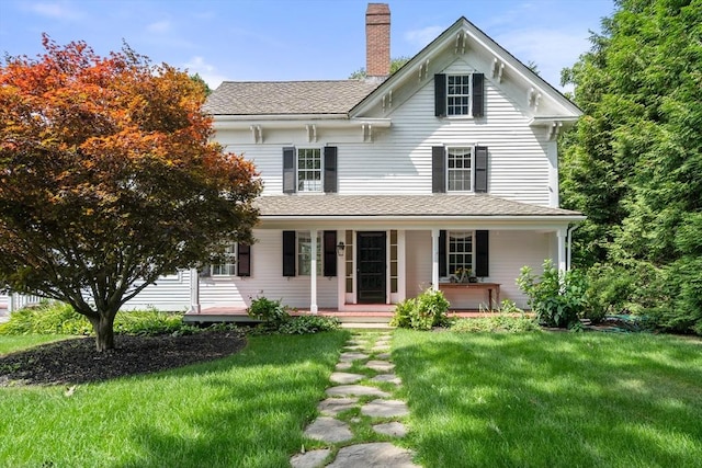 view of front of property featuring covered porch, roof with shingles, a chimney, and a front yard