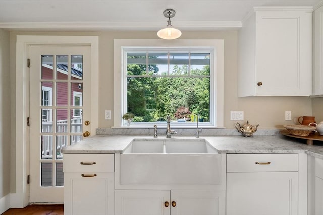 kitchen featuring light stone counters, a sink, white cabinetry, ornamental molding, and pendant lighting