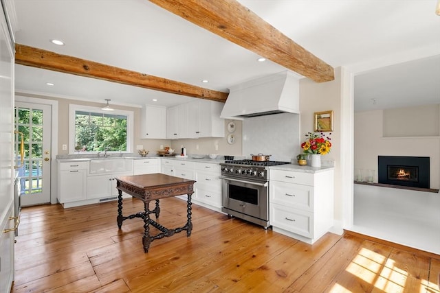 kitchen featuring high end stainless steel range, light countertops, custom range hood, white cabinetry, and a sink