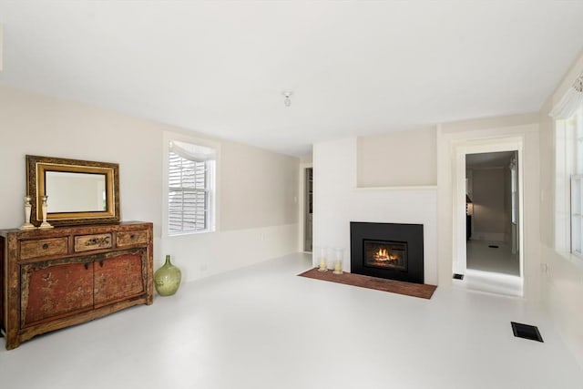 living room featuring concrete flooring, a fireplace with flush hearth, and visible vents