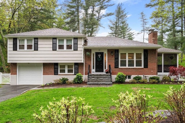 split level home featuring a chimney, asphalt driveway, brick siding, a garage, and roof with shingles