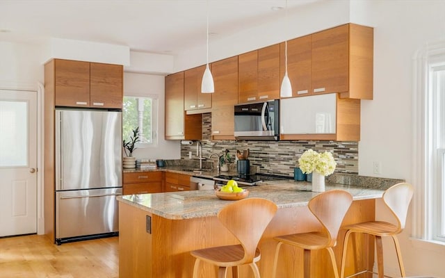 23 Hall Ave Unit 1, Somerville, MA 02144 - kitchen featuring stainless steel appliances, brown cabinets, a peninsula, a sink, and light stone countertops