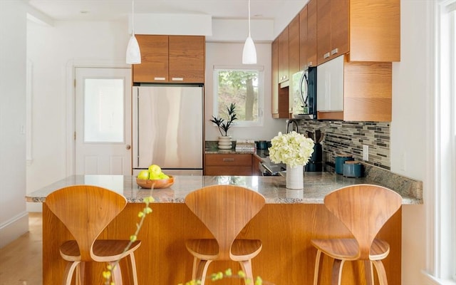 23 Hall Ave Unit 1, Somerville, MA 02144 - kitchen with refrigerator, brown cabinets, a peninsula, decorative backsplash, and pendant lighting
