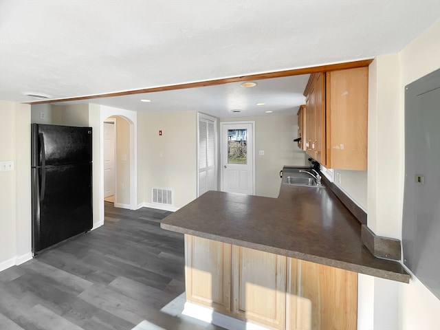 kitchen with black refrigerator, sink, dark hardwood / wood-style flooring, a kitchen bar, and kitchen peninsula