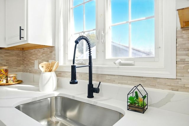 room details with white cabinetry, decorative backsplash, and a sink