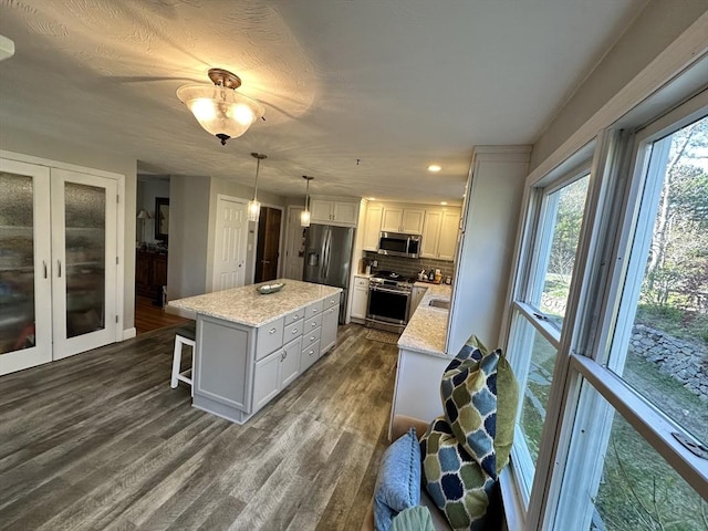 kitchen featuring french doors, a kitchen island, dark wood-style flooring, appliances with stainless steel finishes, and tasteful backsplash